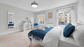 Ein Schlafzimmer mit Bett, Schreibtisch, Stuhl, Spiegel und Fenstern mit Blick auf die Stadt.