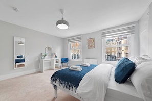 A bedroom with a bed, a desk, a chair, a mirror, and windows with a city view. - Shepherdess Place N1, Old Street, Angel (London)