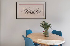 A dining area with a round table, blue chairs, a framed artwork above the table, and a potted plant on the table. - Elmfield Way W9, Westbourne Park, Warrick Ave (London)