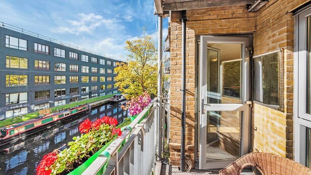 Ein Balkon mit Blick auf einen Kanal, ein Gebäude mit vielen Fenstern und eine Tür zu einem Zimmer.