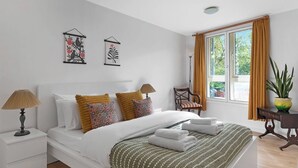 Ein Hotelzimmer mit Bett, Nachttischlampen, einem Sessel, einem Fenster mit Vorhängen und Wandbildern.
