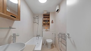 Ein modernes Badezimmer mit Badewanne, Toilette und Dusche. Ein Ablagefach mit Pflegeprodukten und ein Spiegel über dem Waschbecken.