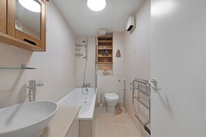 A modern bathroom with a bathtub, toilet, and shower. There is a shelf with toiletries and a mirror above the sink. - Elmfield Way W9, Westbourne Park, Warrick Ave (London)