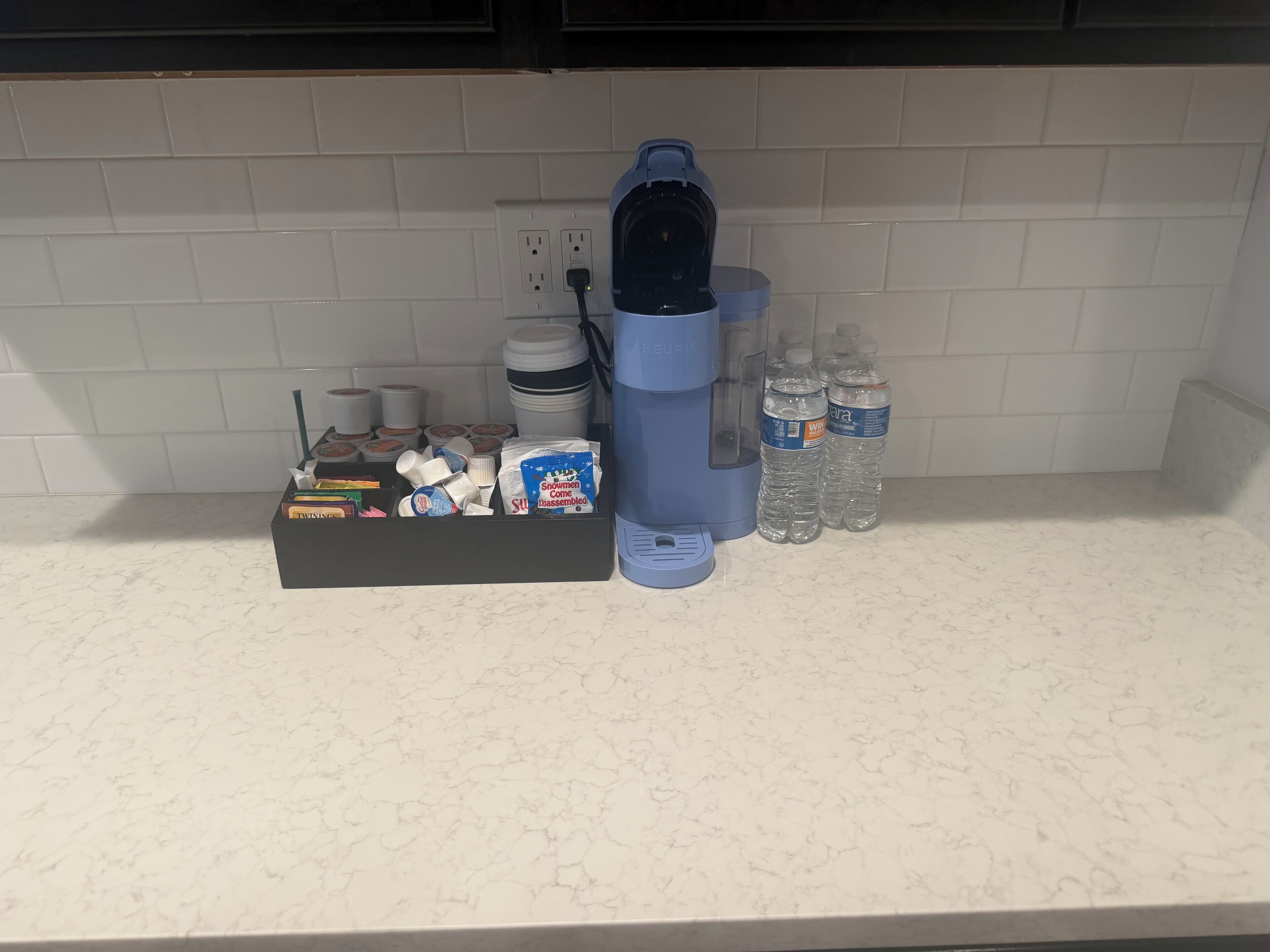 A kitchen counter with a coffee maker, water bottles, and a box of snacks.