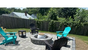 Ein Außenbereich mit Terrasse, einem Feuerkorb, zwei türkisfarbenen Adirondack-Stühlen und einem schwarzen Stuhl.