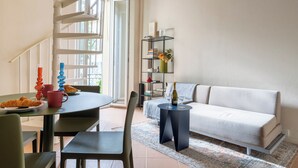Ein modernes Wohnzimmer mit einer Couch, einem Esstisch mit Stühlen, einer Treppe und einem Bücherregal.