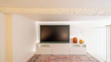 Una sala de estar moderna con un televisor de pantalla plana montado en un mueble blanco, un tapete estampado y una mesita con objetos decorativos.