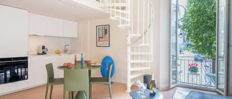 A modern kitchen with white cabinets, a dining area with green chairs, a blue table, and a spiral staircase.