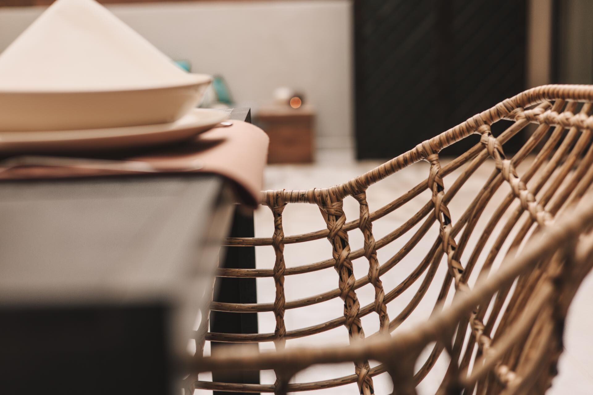 A wicker chair with a woven backrest and a table with a white plate and a black object.