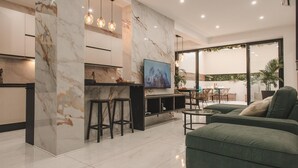 Ein modernes Wohnzimmer mit einem grünen Sofa, einem an der Wand befestigten Fernseher und einer Küchenzeile mit Marmorarbeitsplatten.