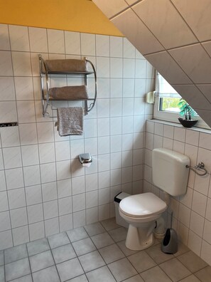 A small bathroom with a toilet, a towel rack with two towels, a window, and a potted plant on the windowsill. - Your "home port" in Butjadingen - spacious family apartment with pool*sauna*dogs (Butjadingen)