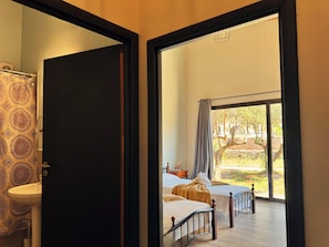A bedroom with a large window, a bed, a bedside table, and a bathroom with a patterned shower curtain.