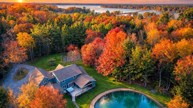 A house with a swimming pool, surrounded by autumn foliage and a view of a lake.