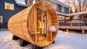 A wooden sauna structure with a bench and a towel rack, set on snow-covered ground.