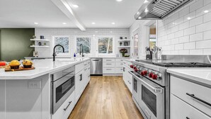 A modern kitchen with white cabinetry, stainless steel appliances, and a wooden floor.