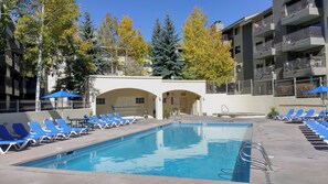 A pool area with blue lounge chairs and a clear blue pool. - Remodeled Condo w/ FREE WiFi, Parking, Heated Pool, Hot Tubs, Skier Shuttles (Avon)