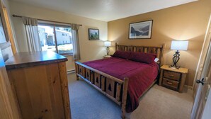 A bedroom with a wooden bed, two bedside tables with lamps, a window with curtains, and two framed pictures on the wall. - Remodeled Condo w/ FREE WiFi, Parking, Heated Pool, Hot Tubs, Skier Shuttles (Avon)