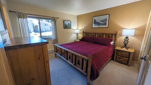 A bedroom with a wooden bed, two bedside tables with lamps, a window with curtains, and two framed pictures on the wall. - Remodeled Condo w/ FREE WiFi, Parking, Heated Pool, Hot Tubs, Skier Shuttles (Avon)