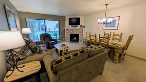 A living room with a fireplace, a television, and a dining area with wooden chairs and a table. - Remodeled Condo w/ FREE WiFi, Parking, Heated Pool, Hot Tubs, Skier Shuttles (Avon)