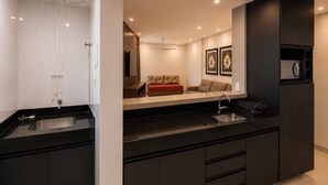Una cocina moderna con encimera negra, pileta de acero inoxidable y microondas integrado.