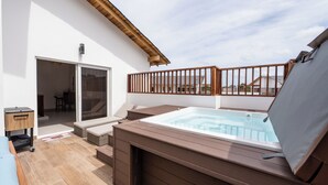 Eine Dachterrasse mit Whirlpool, Sitzgelegenheit und einer Schiebetür zu einem Innenbereich.