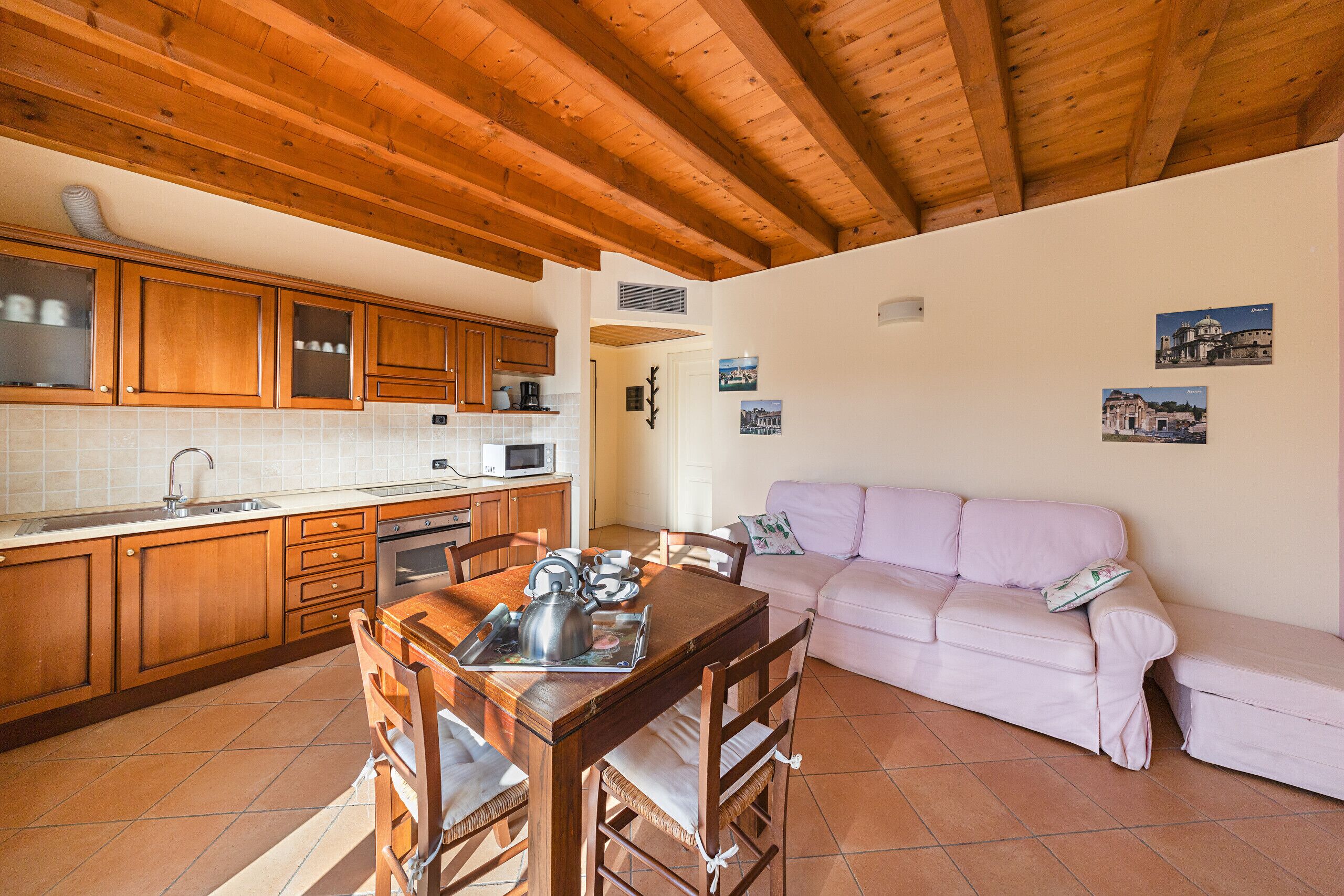 Eine Küche mit Holzausstattung, einem Esstisch mit Stühlen, einem rosa Sofa und Fliesenboden.