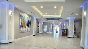 Un passadís d'hotel espaiós amb un disseny de sostre modern, un gran quadre abstracte a la paret esquerra i una zona de recepció a la distància.