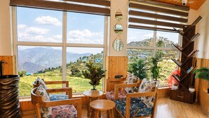 A room with large windows, wooden furniture, and a view of a mountainous landscape. - Hotel Amadeus (Tehri)