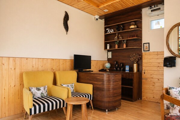 A cozy room with wooden paneling, a yellow armchair, a striped bench, a small wooden table, a TV, a globe, and a coffee machine. - Hotel Amadeus (Tehri)