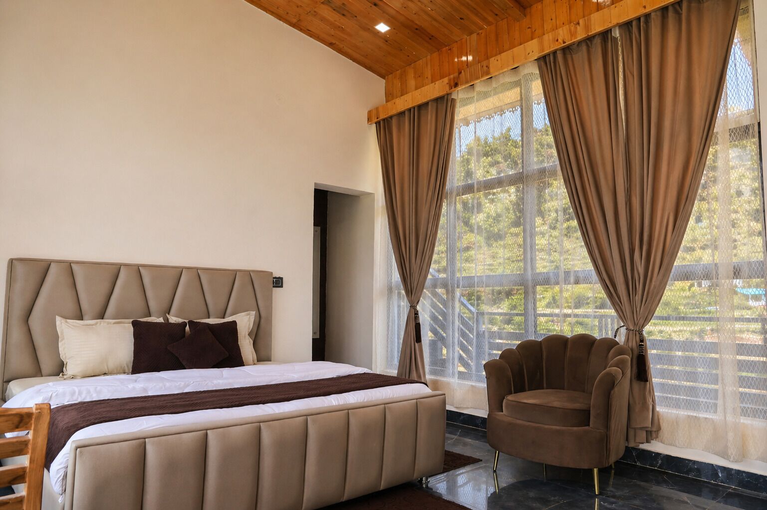 Quarto com uma cama grande, uma cadeira e vista pela janela com cortinas.