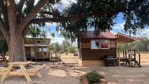 A rustic cabin with a wooden exterior, a small porch, and a grill area. - Bob White Tiny Cabin (Quitaque)
