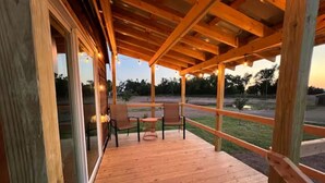A wooden deck with a pergola, outdoor seating, and a view of the surrounding landscape. - Bob White Tiny Cabin (Quitaque)