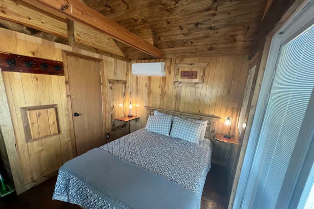 Ein Zimmer mit Holzboden, einem Bett, einer Tür und einem Fenster.