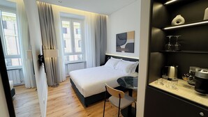 A modern hotel room with a large bed, a desk with a coffee maker, and a chair. - Eternal Suites Rome (Rome)