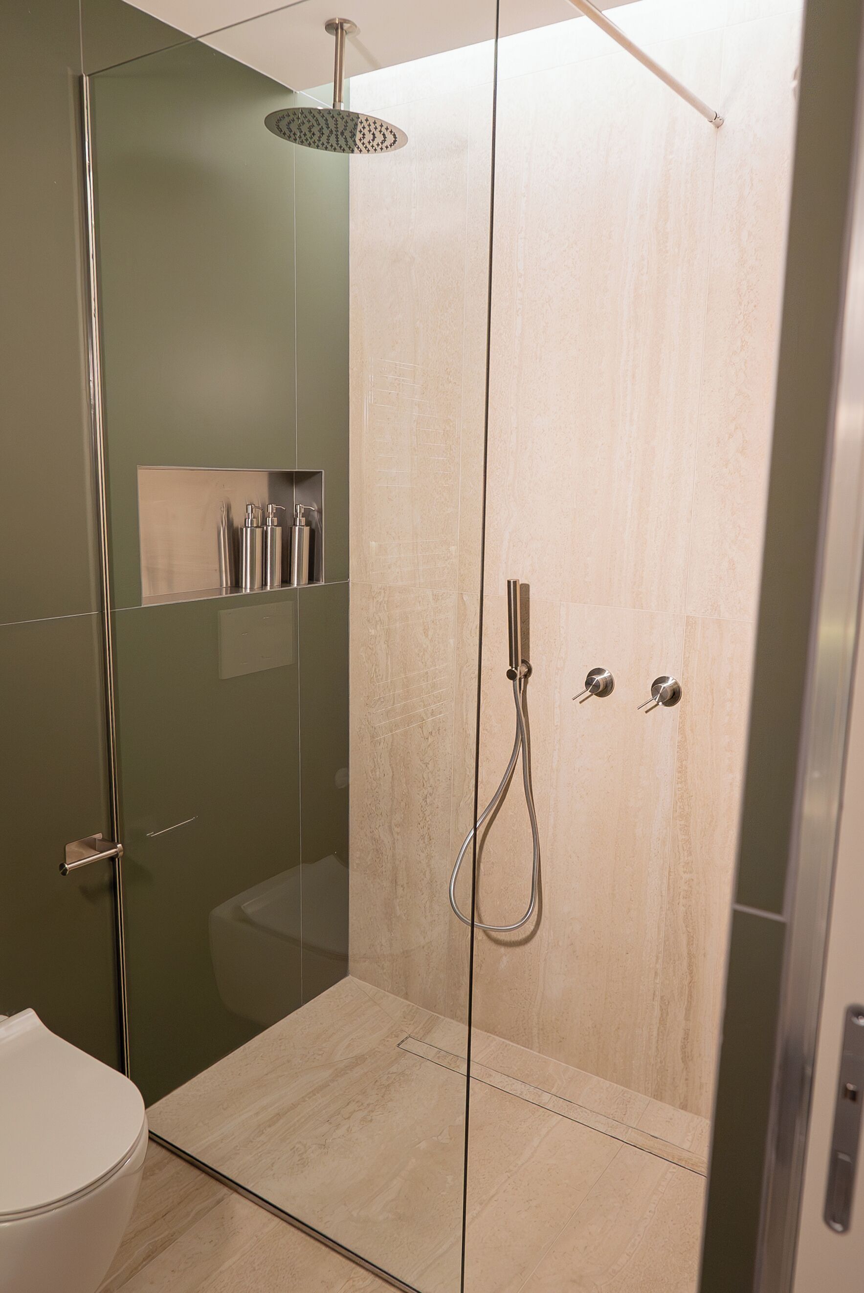 Une salle de bain moderne avec une douche à parois de verre, des toilettes et une étagère contenant des articles de toilette.