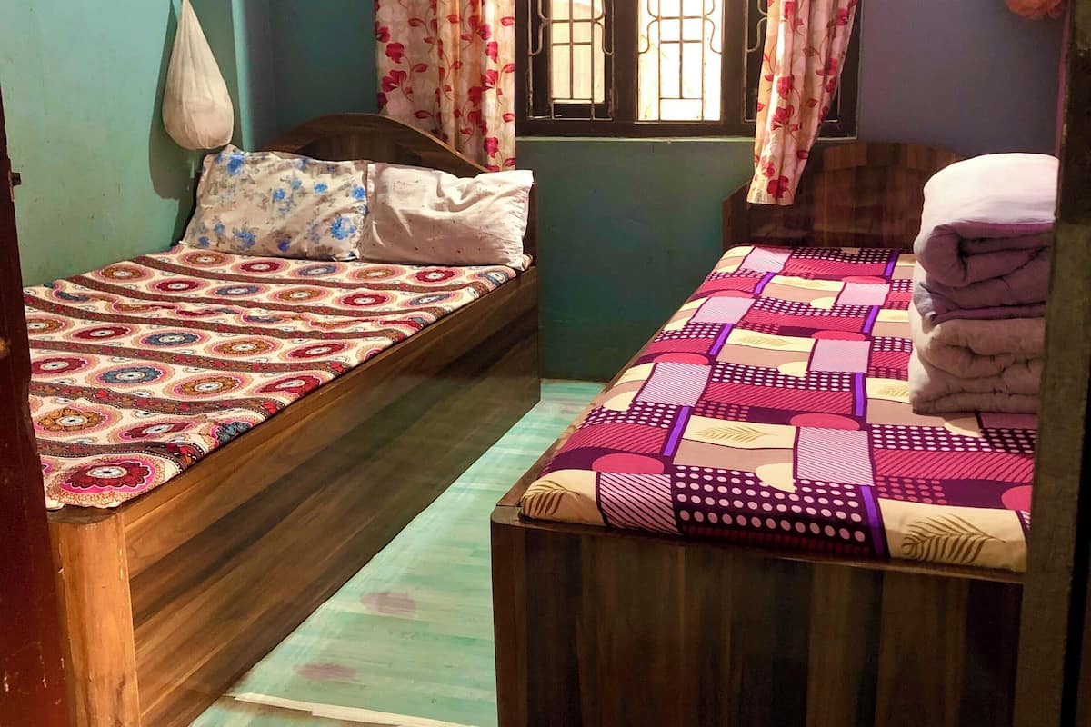 Una habitación con dos camas de madera, cada una con una colcha estampada. Se ve una ventana con barrotes y cortinas con motivos florales.