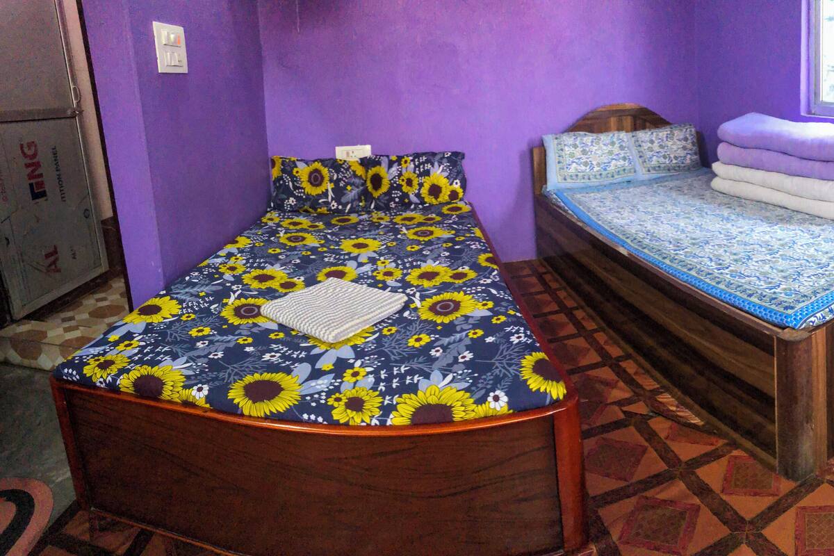 Una habitación con una cama con colcha floral, una mesita con toallas dobladas y una ventana con cortinas.