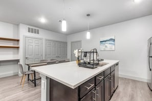 A modern kitchen with a central island, built-in cabinets, and a dining area with chairs. - Grand Prairie 2BR | IKEA, Epic Waters, Bass Pro (Grand Prairie)