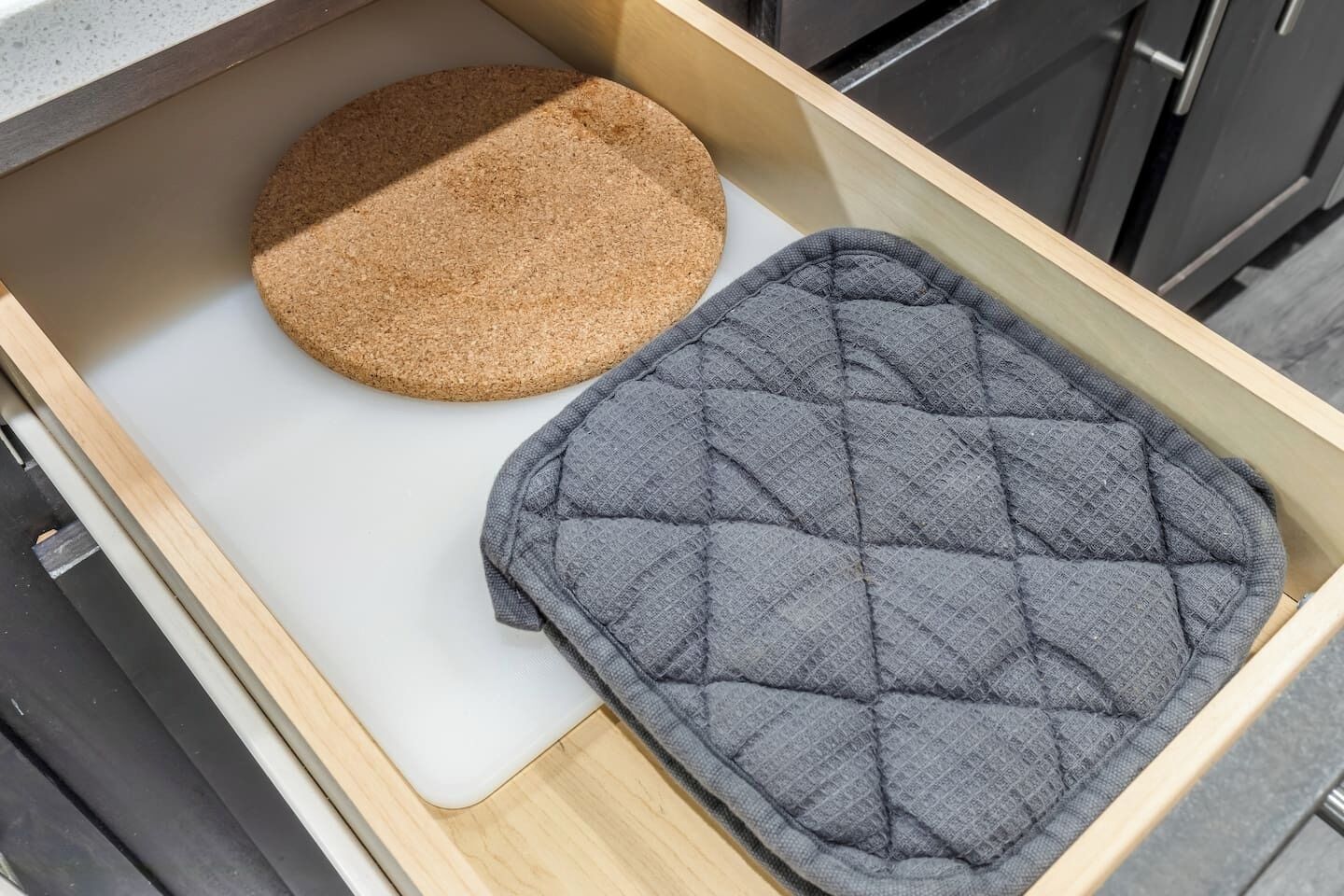 A kitchen drawer containing a round cork mat and a grey quilted mat.