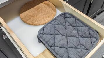 A kitchen drawer containing a round cork mat and a grey quilted mat.