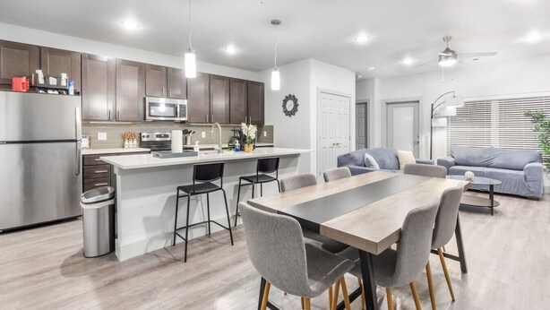 Een moderne keuken met een centraal eiland, roestvrijstalen apparatuur en een eethoek met een houten tafel en stoelen.