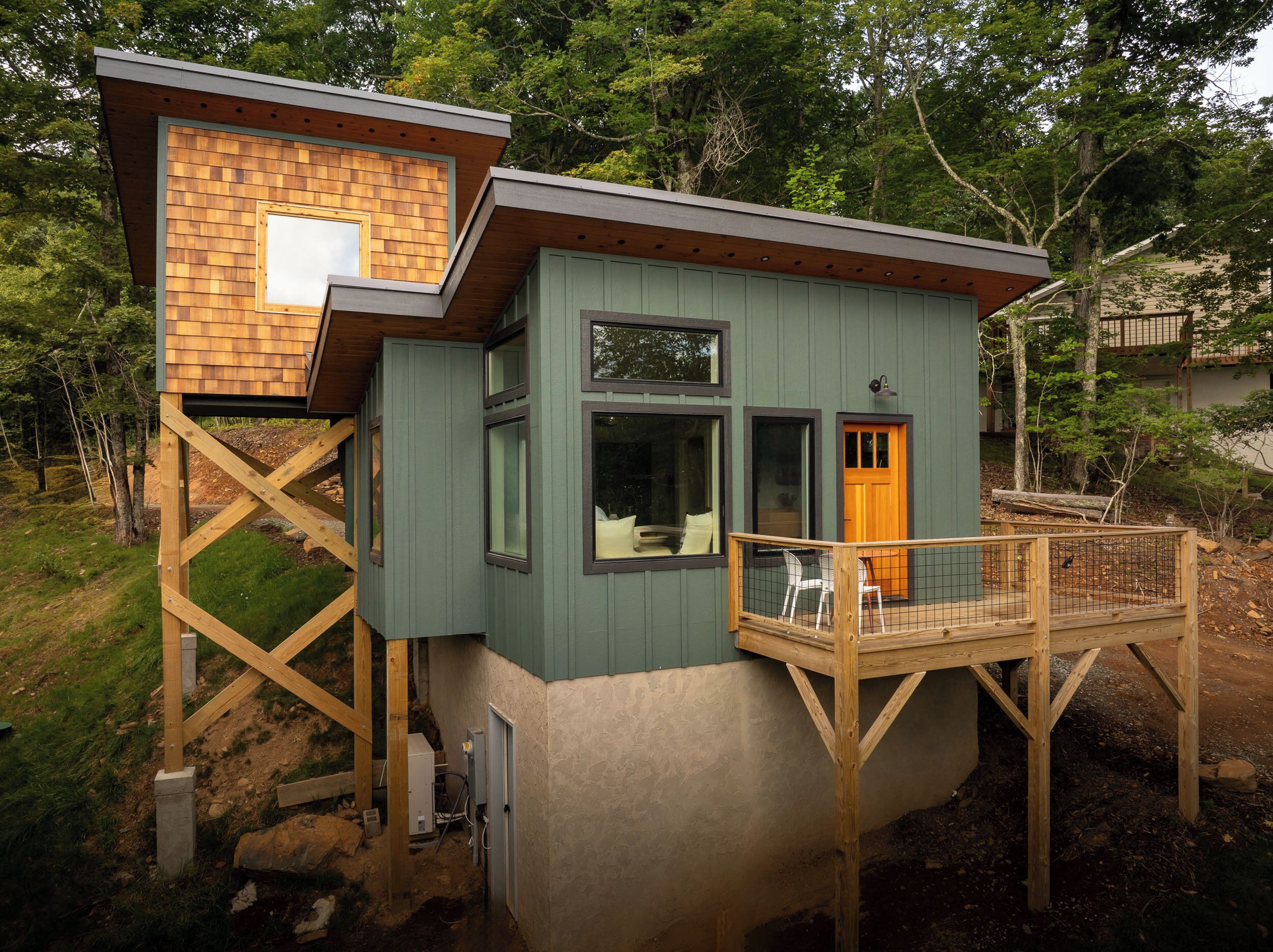 A two-story wooden cabin with a balcony, a wooden deck, and a small enclosed porch area.