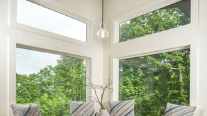 A round dining table with a vase centerpiece, surrounded by two bench seats with patterned cushions, set against a backdrop of large windows overlooking a forest. - the Birdhouse of Boone, Luxe + Long Views + Charming Tiny Home (Boone)