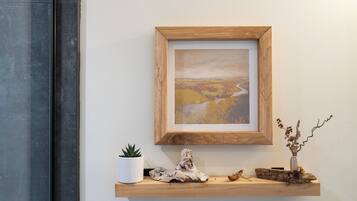 Un tableau représentant un paysage, encadré et accroché au mur, une petite plante en pot et un objet décoratif en bois posé sur une étagère.