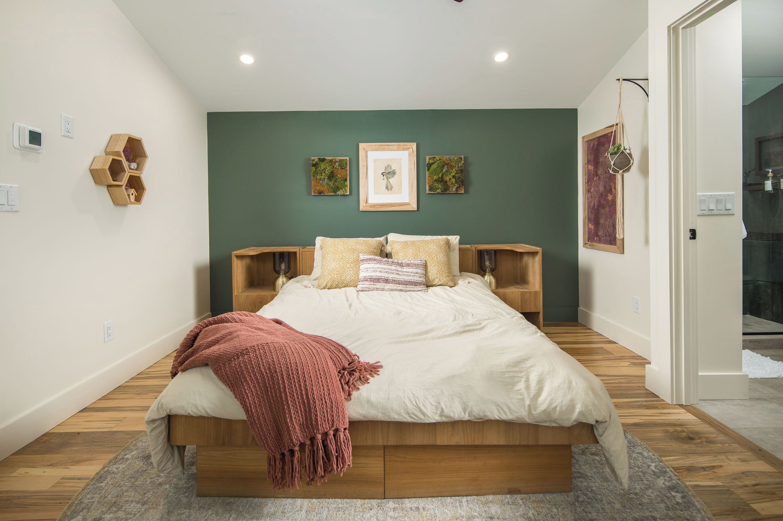 A bedroom with a bed, wooden headboard, a green accent wall, and a small wooden shelf.