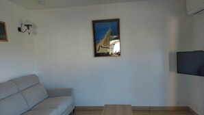 Un saló amb un sofà gris, una taula de centre de fusta, un quadre amb marc i una televisió de pantalla plana.
