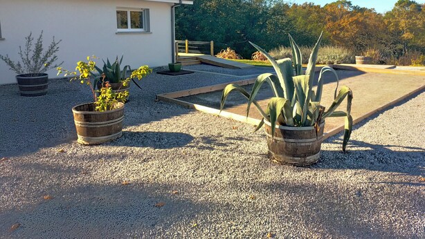 Una casa amb teules al sostre i un camí de grava. Hi ha diverses plantes en testos al davant de la casa.