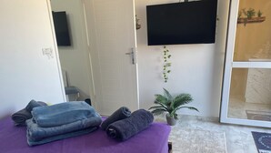 Een kamer met een bed belegd met paarse en blauwe handdoeken, een bloempot, een flatscreen-televisie aan de muur en een schuifdeur naar een buitenruimte.