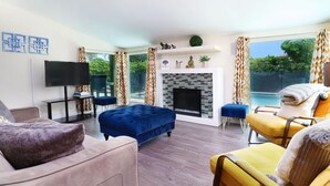 Een moderne woonkamer met een open haard, een flatscreen televisie en een groot raam met uitzicht op een zwembad.