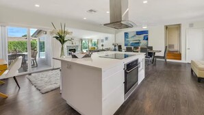 Een moderne keuken met een centraal kookeiland, een eethoek met tafel en stoelen, en een groot raam met uitzicht op de omgeving.